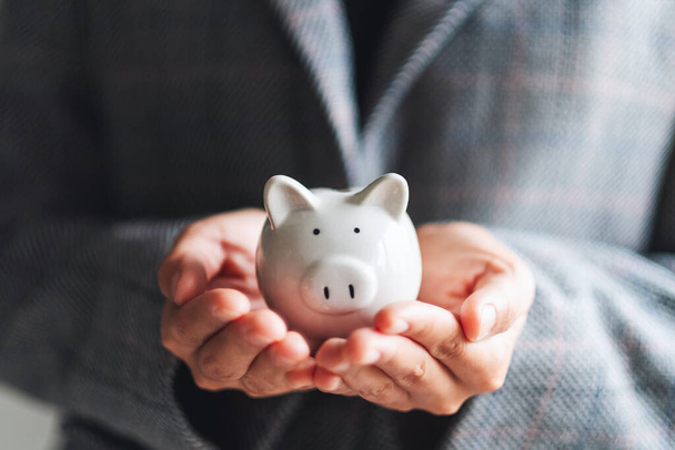 Close-up imago van een zakenvrouw die een spaarvarken vasthoudt voor het besparen van geld en financieel concept - Foto, afbeelding