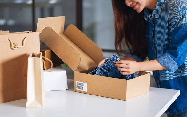 A beautiful young asian woman receiving and opening a postal parcel box of clothing at home for delivery and online shopping concept - Photo, image