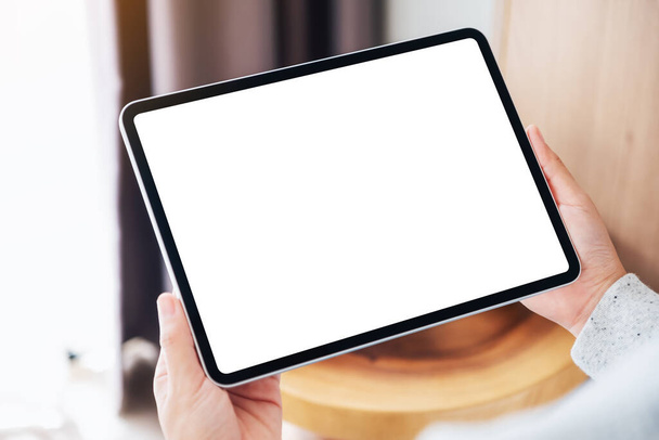 Mockup image of a woman holding black tablet pc with blank desktop white screen while sitting on a cozy white bed at home - Photo, Image