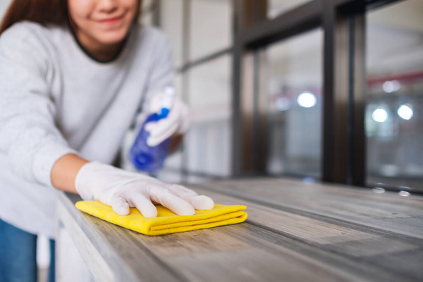 Μια νεαρή γυναίκα που φοράει προστατευτικό γάντι καθαρίζει το τραπέζι για τις δουλειές του σπιτιού - Φωτογραφία, εικόνα