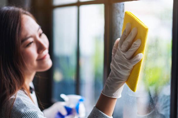 Una giovane donna che indossa un guanto protettivo pulisce la finestra per il concetto di lavori domestici - Foto, immagini