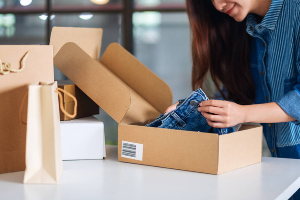 A beautiful young asian woman receiving and opening a postal parcel box of clothing at home for delivery and online shopping concept - Fotoğraf, Görsel