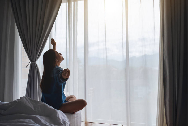 Молода жінка робить розтягування після пробудження вранці на білому затишному ліжку вдома
 - Фото, зображення