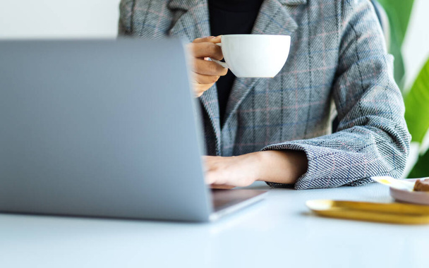 Zbliżenie wizerunku bizneswoman pracującej i korzystającej z laptopa podczas picia kawy w biurze - Zdjęcie, obraz