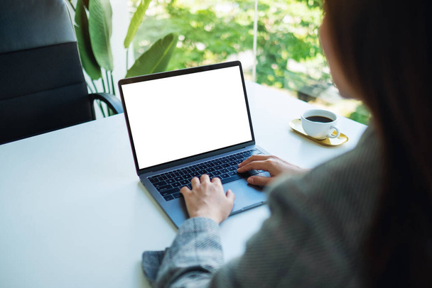 Mockup beeld van een zakenvrouw met behulp van en typen op laptop toetsenbord met blanco witte desktop scherm in het kantoor - Foto, afbeelding