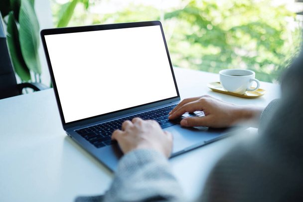 Mockup immagine di una donna d'affari che utilizza e digita sulla tastiera del computer portatile con schermo bianco vuoto desktop in ufficio - Foto, immagini