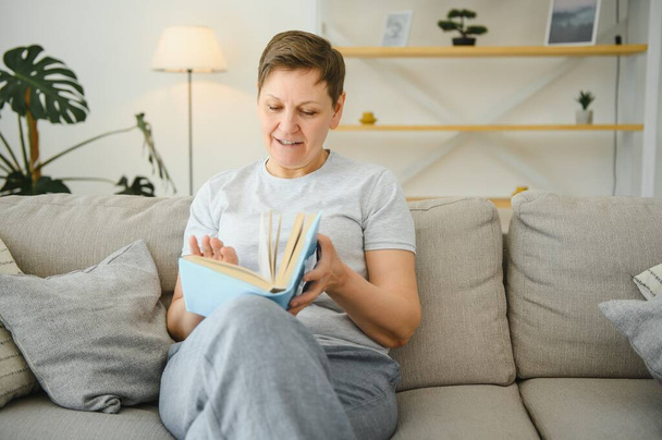 woman in home sitting on sofa reading book - Фото, изображение