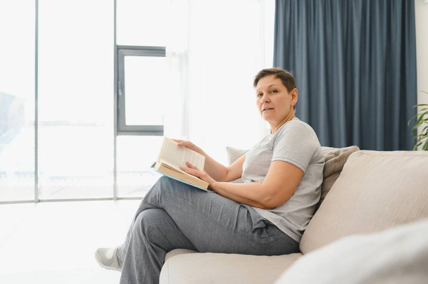 kobieta w domu siedzi na kanapie czytanie książki - Zdjęcie, obraz