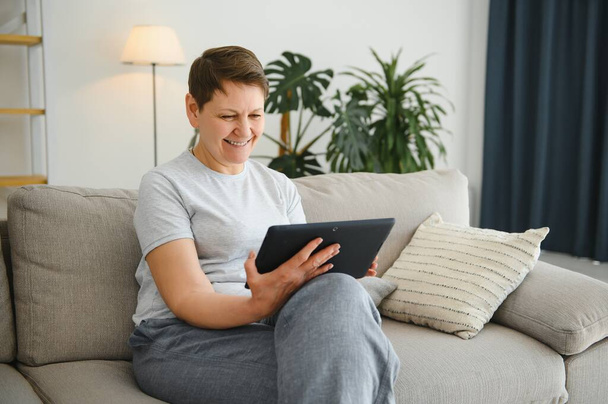 people, technology and internet concept - happy middle aged woman with tablet pc computer at home - Foto, afbeelding