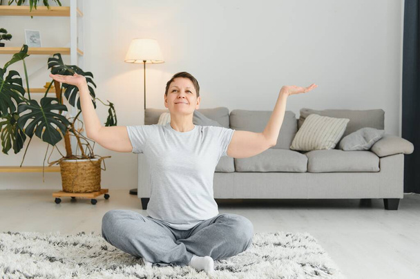 Middle-aged woman doing yoga at home for stretching and being healthy - Fotografie, Obrázek
