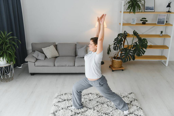 Adult woman doing fitness exercises at home. Senior woman do stretching exercises. Mature woman doing yoga poses. - Фото, изображение