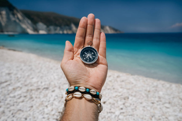 Hand holding a compass on the beach in background. - Фото, изображение