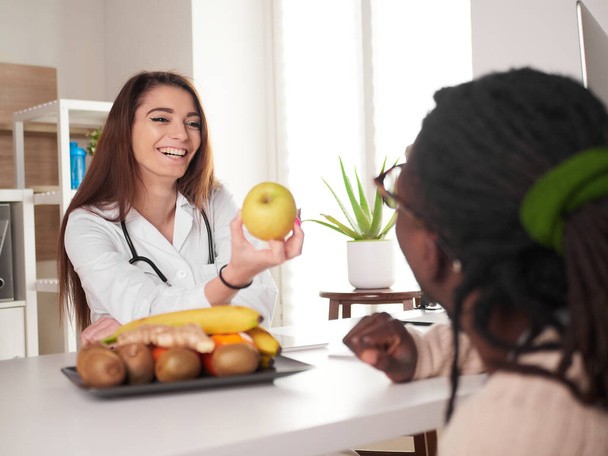 young female nutritionist in office show a green apple to her patient - Fotó, kép