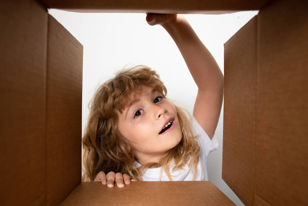 Kid unpacking and opening carton box, and looking inside with surprise face. Unpacking cardboard box for kids. - Fotografie, Obrázek