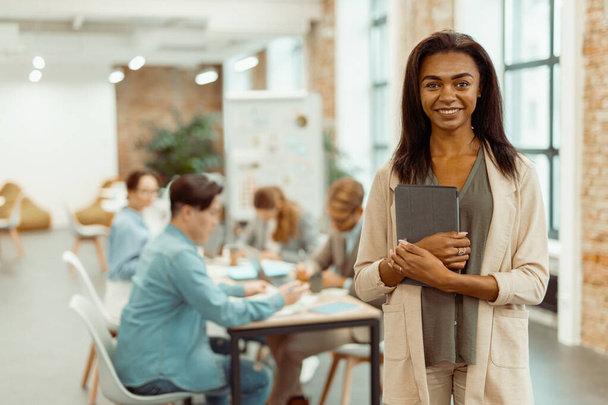 glimlachende jonge vrouw staan met gadget in het kantoor - Foto, afbeelding