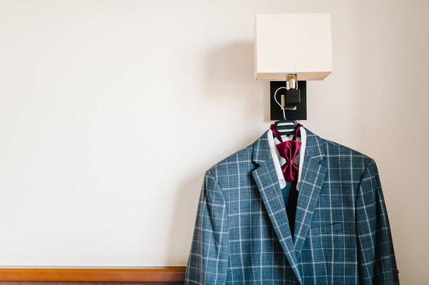 A man's jacket, blue suit with bow-tie on a hanger in the room. Stylish blue wedding. - Photo, Image