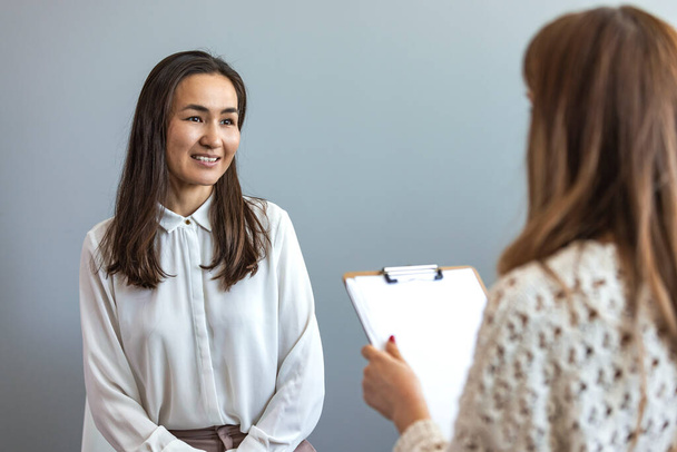 Successful psychologist talking to her patient. Positive young female therapist gestures as she talks with a female client. The therapist smiles warmly as she talks with the young woman. - Foto, Bild