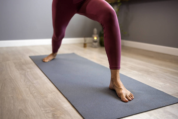 Athletic woman practices yoga, does one Warrior exercise, Virabhadrasana 1 pose, exercises, wears sportswear, indoors, yoga studio up close. The concept of a healthy lifestyle.  - Foto, Imagen