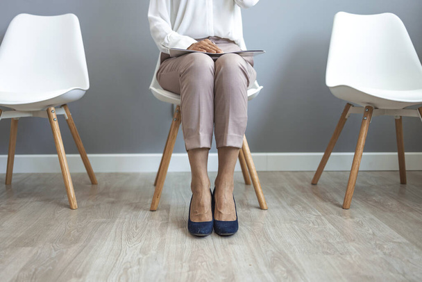 Young woman waiting for job interview in reception hall. Woman sitting on chair in waiting room, setting her mind up before job interview or meeting with potential business partners - Фото, изображение