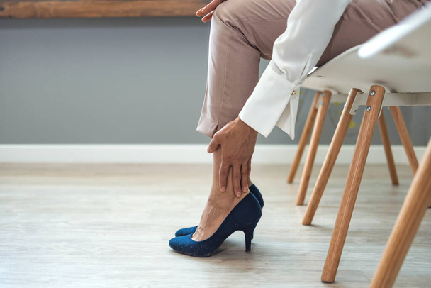 Health care concept. Woman suffering from pain in heel, closeup. Woman suffering from leg pain in office. Closeup of tired businesswoman woman sitting on chair and massaging feet - Foto, Imagem