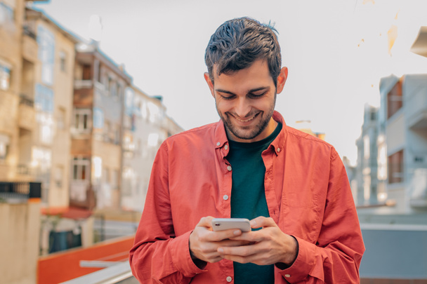 человек с мобильным телефоном на улице в красной рубашке в случайном стиле - Фото, изображение