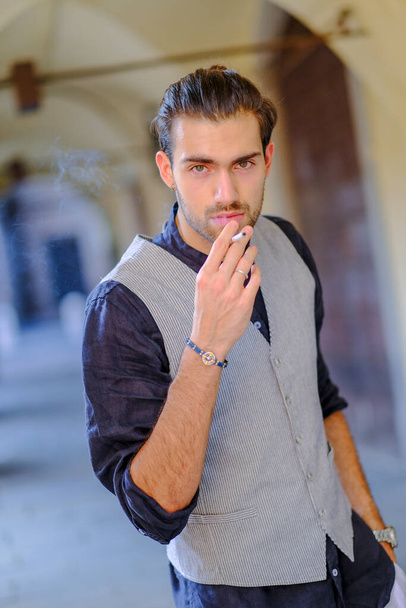 beautiful Italian dark-haired guy with shirt and vest smokes on the street. High quality photo - Photo, Image
