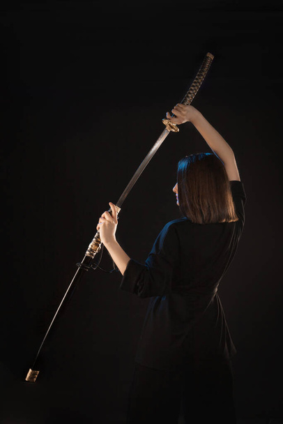 A young beautiful woman in a black kimono draws a Japanese katana from its scabbard, back view. - Fotó, kép