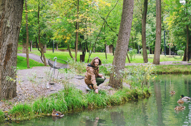 Młoda szczęśliwa kobieta spacerująca w deszczu w zielonym parku z parasolem, uśmiechnięta, zabawna. osoba siedząca na ławce. Zimna pogoda. Wiosną. Spadek. - Zdjęcie, obraz