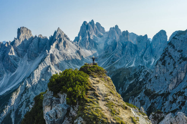 Aerial view of a woman hiker raising her hands on mountain top enjoying Cadini di Misurina mountain peaks, Italian Alps, Dolomites, Italy, Europe. - Zdjęcie, obraz