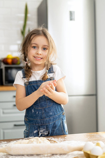 Cute toddler girl cooking and looking at the camera. Kid spends leisure at home, baking cookies, enjoying weekend - Foto, Bild