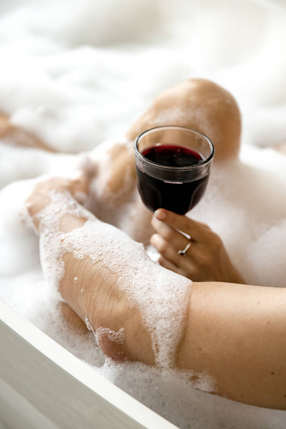 Girl holding a glass of wine in her hand enjoying a bubble bath with her boyfriend. High quality photo - Photo, image