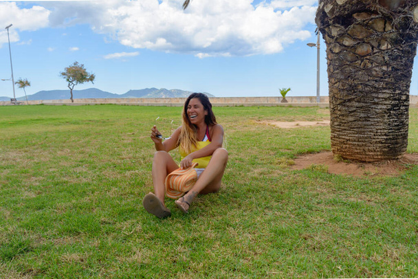 portrait d'une femme latine souriante, s'amusant, en vacances à Mallorca posant par une chaude journée de printemps été, sous un palmier, concept de vacances - Photo, image