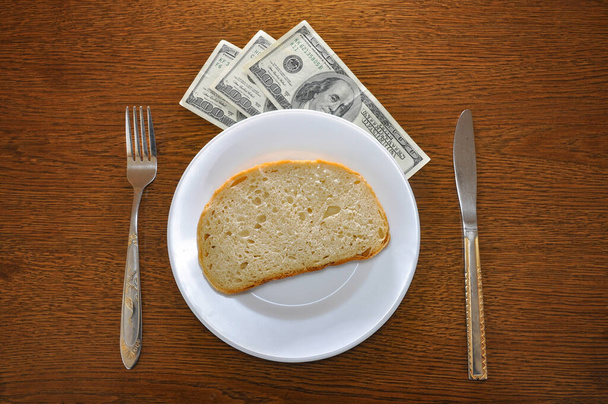 Тарелка с куском хлеба и под тарелкой американские доллары. Фотография предполагает проблему роста цен в мире - Фото, изображение
