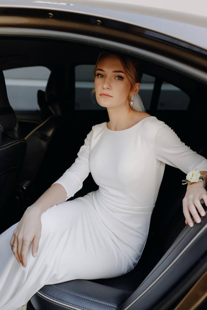 Gyönyörű, stílusos menyasszony ül az autóban, és a kamerába néz. Kiváló minőségű fénykép - Fotó, kép