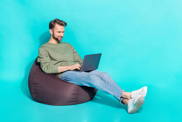 Full size photo of young blond guy type laptop wear sweater jeans shoes isolated on turquoise background - Foto, afbeelding