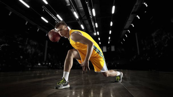One young basketball player in action and motion in flashlights over dark gym background. Concept of sport, energy and dynamic, healthy lifestyle. Arenas drawned - Foto, Bild