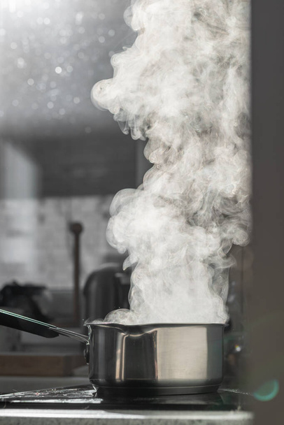 Boiling water with steam in a pot on an electric stove in the kitchen. Blurred background, selective focus. - Фото, изображение