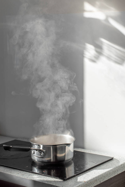 Acqua bollente con vapore in una pentola su una stufa elettrica in cucina. Sfondo sfumato, messa a fuoco selettiva. - Foto, immagini