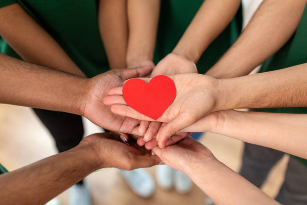 close up of volunteerss hands holding red heart - Foto, afbeelding