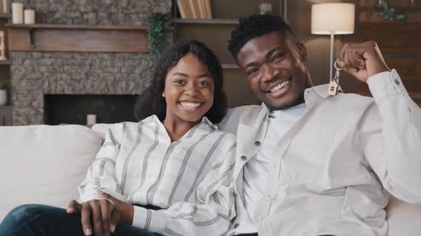 Afrikanisches Ehepaar sitzt in modernem Wohnzimmer im neuen Heim Frau und Mann zeigen Schlüsselbund von neuen Luxus-Haus-Wohnung gemietet. Eigenheimbesitzer mit Hypothekenkredit - Filmmaterial, Video