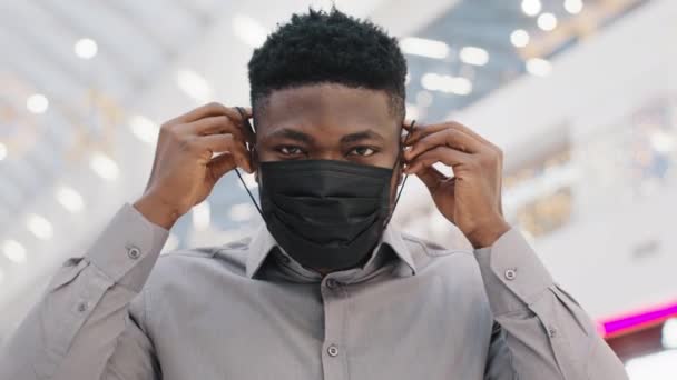 Nahaufnahme junger afrikanisch-amerikanischer Mann trägt medizinische Schutzmaske beobachtet Vorsichtsmaßnahmen während Pandemie Blicke in die Kamera zeigt ok Geste Genehmigung Symbol unterzeichnen Vereinbarung schützen Ihre Gesundheit - Filmmaterial, Video