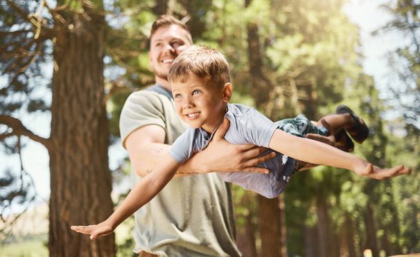 Flying with dad. Cropped shot of a handsome young man playing with his adorable little son while camping in the woods. - 写真・画像