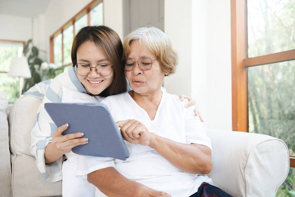 Fogantatás szeretet és gondozás az idősek, egy idős ázsiai nő nézi a tabletta által mutatott lánya. - Fotó, kép