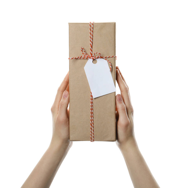 Woman holding parcel wrapped in kraft paper with tag on white background, closeup - Фото, изображение