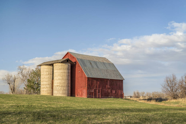 old red barn with twin silo and irrigation ditch at Colorado foothills, early spring scenery at sunset, public Shenandoah Park in Fort Collins - Foto, Imagen