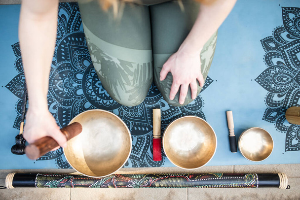 Yoga concept, meditation and sound therapy. Beautiful young caucasian woman surrounded by copper tibetan singing bowls and instruments. - Photo, Image