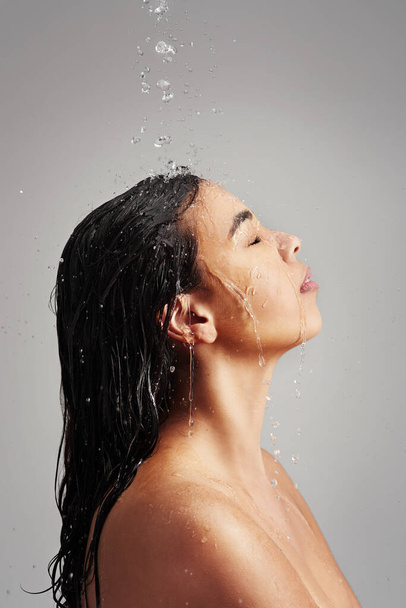 Wat een geweldige manier om de dag te beginnen. Studio shot van een jonge vrouw genieten van een douche tegen een grijze achtergrond. - Foto, afbeelding