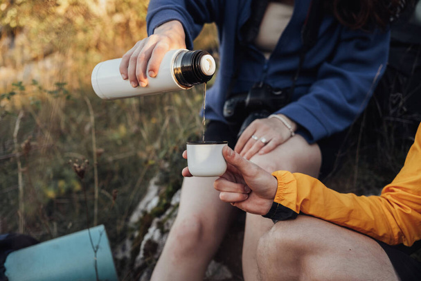 二人の旅行者男と女は魔法瓶から熱いお茶を飲むためにハイキング中に停止しました - 写真・画像