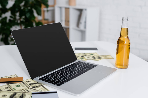 ноутбук з порожнім екраном біля кредитних карток, доларів і пляшки пива
 - Фото, зображення