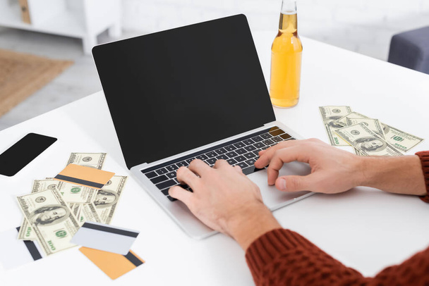 partial view of gambler typing on laptop with blank screen near dollars and credit cards - Photo, Image